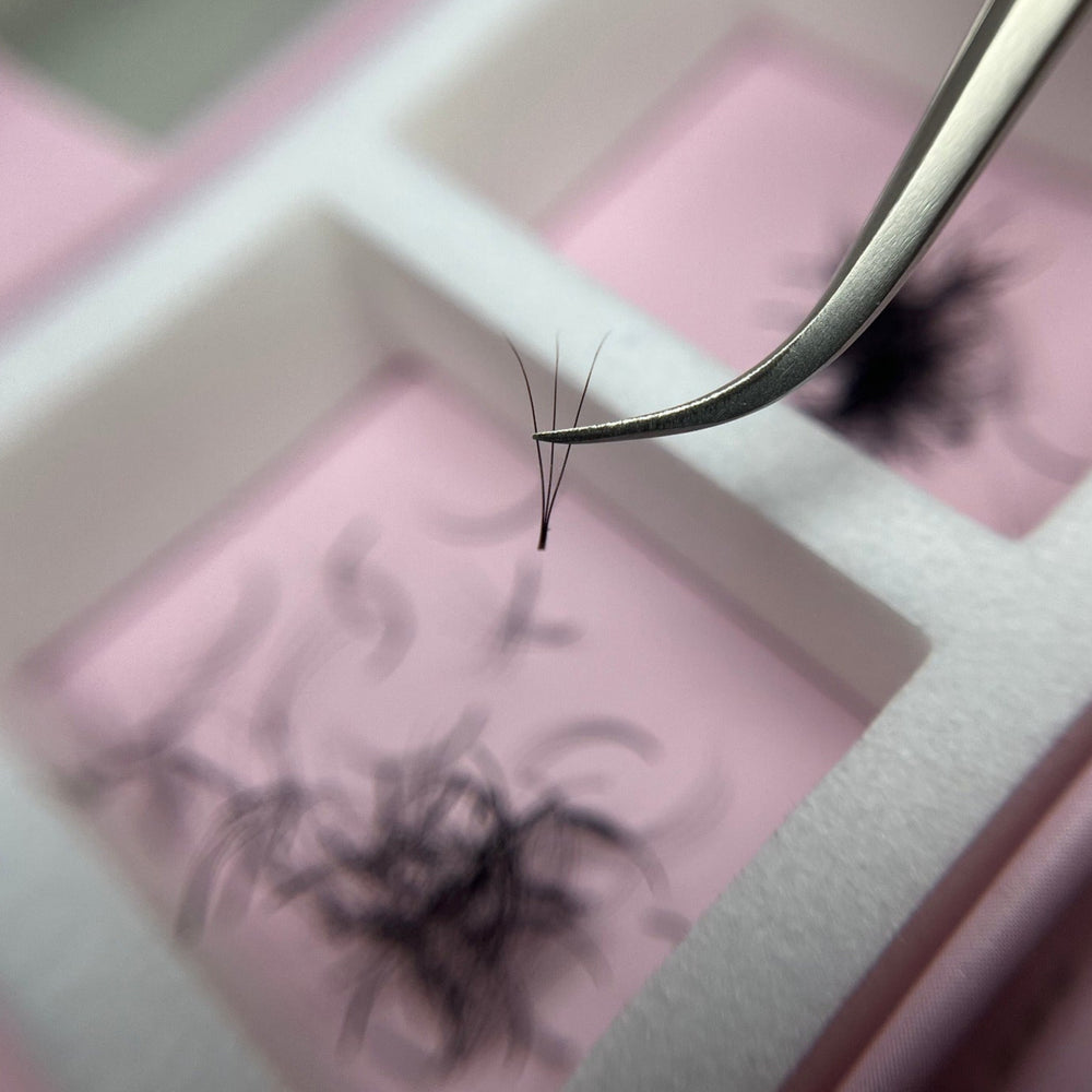 Eyelash extension process with tweezers and false eyelashes on a pink tray.