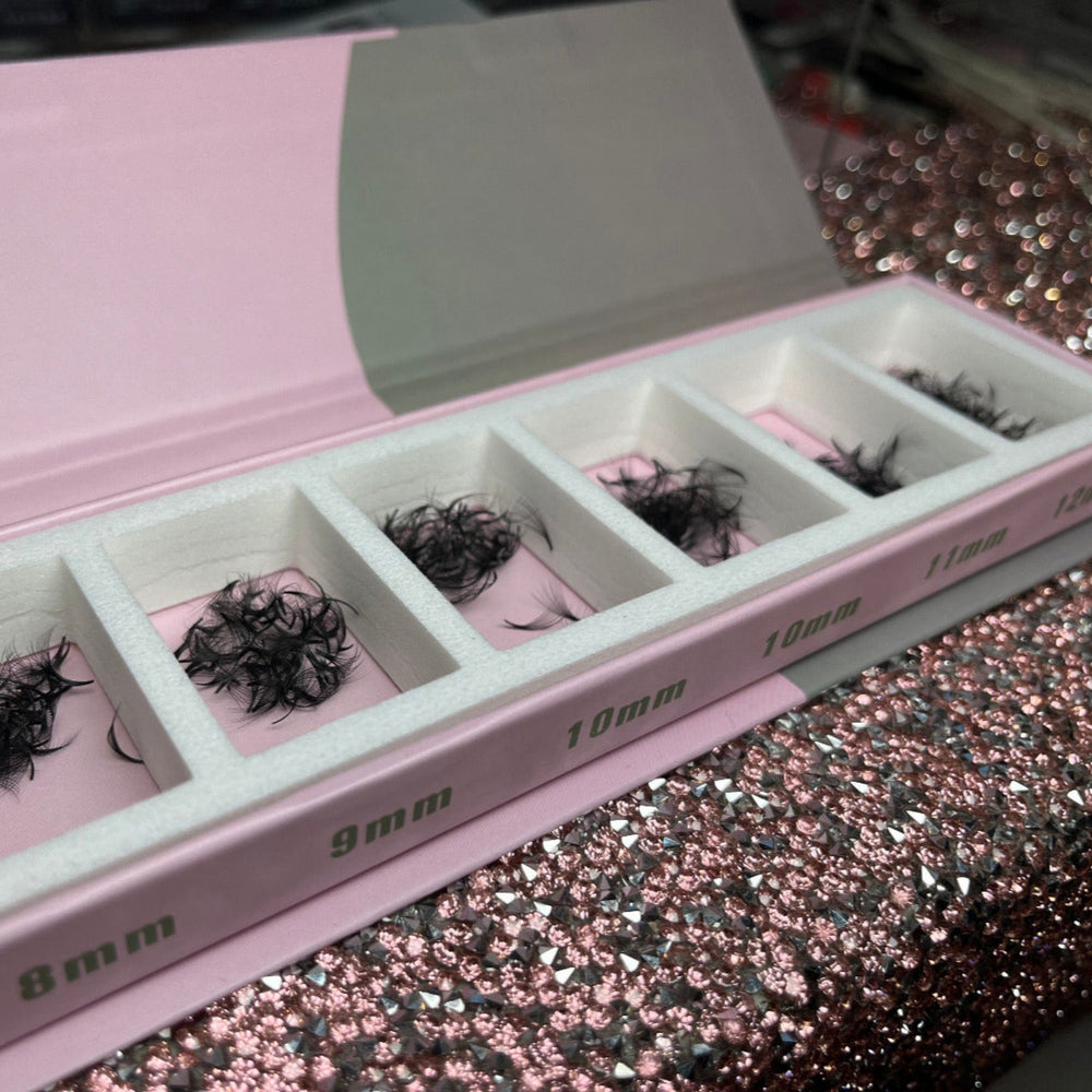 Box with compartments containing black eyelash extensions on a glittery surface